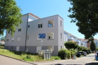 Gebäudezeile mit 4 Etagen, hellgraue Fassade. Blick von Straße auf gepflasterten Privatweg in Innenhof.