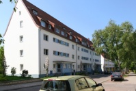 Altbauten mit Spitzdach, 4 Etagen, Vorgärten begrünt. Fassade weiß mit blauen Akzenten. Straße.
