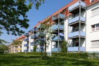 Altbauten mit sanierten Fassaden in weiß und angebauten Balkonen in gelb, blau und rot. Davor Grünfläche, Bäume.