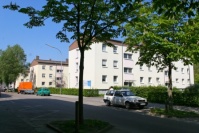 Mehrere Gebäude hintereinander mit drei Etagen, quer zur Straße, Grünflächen dazwischen. Vorne Bäume.