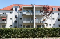 Sanierter Altbau mit Anbau über 3 Etagen, oben Dachterrasse. Fassade hellblau, Bäume und Hecken.