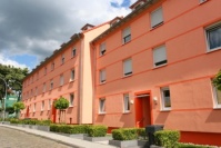 Sanierter Altbau mit drei Wohnetagen, Fassade in orange. Vorgärten sind mit niedrigen Hecken eingefasst.