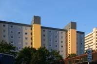 Sanierter Wohnblock, Flachdach, 9 Etagen. Fassade in hellen Blautönen. Treppenhaustürme gelb. Davor 