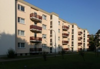 Gebäudezeile 4 Etagen, Flachdach, Fassade hell, rote Balkone. Davor Wiese.