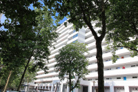 Ausschnitt Hochhaus mit weiß-grau gestreifter Fassade, vorne Blätter von Bäumen