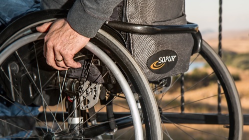 Ein Mensch in einem Rollstuhl Eine Hand hält das Rad eines Rollstuhls