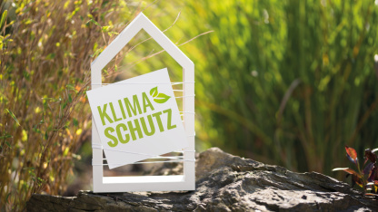 Klimaschutz-Symboldbild Weißes Haus mit der Aufschrift Klimaschutz umgeben von Pflanzen