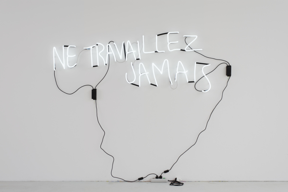 Light tubes on white wall form text "Ne travaillez Jamais"