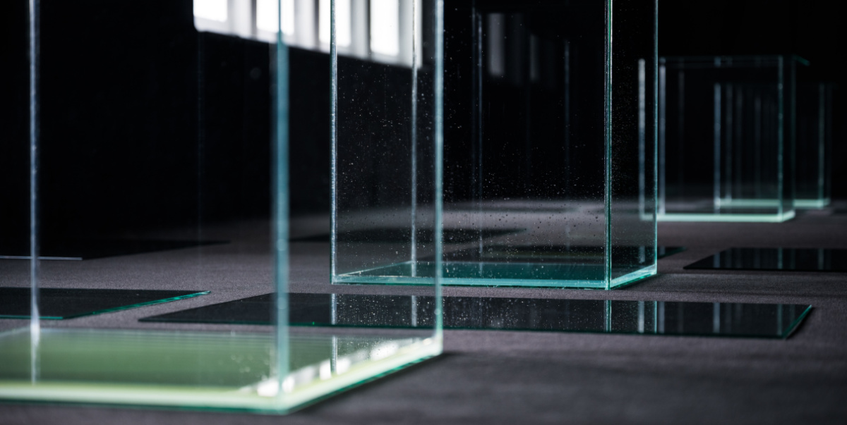 Raum mit schwarzem Molton ausgelegt, große Glaskuben auf dem Boden mit Wasser befüllt. Das Wasser steht 2 CM hoch.