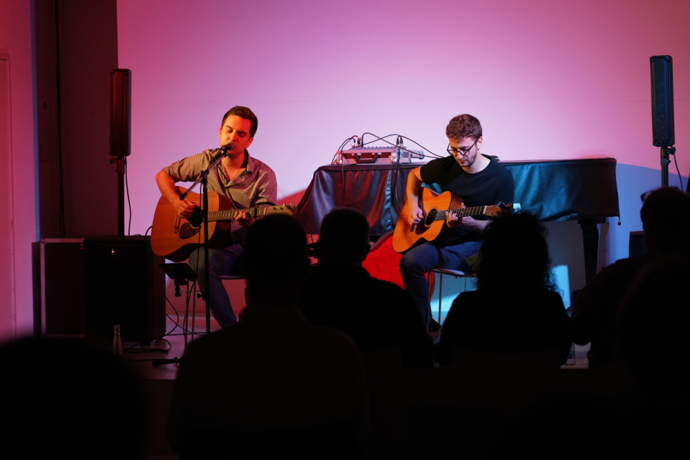 Veranstaltungsraum der Stadtgalerie, Umrisse von einem Publikum, zwei männliche Gitarrenspieler auf der Bühne