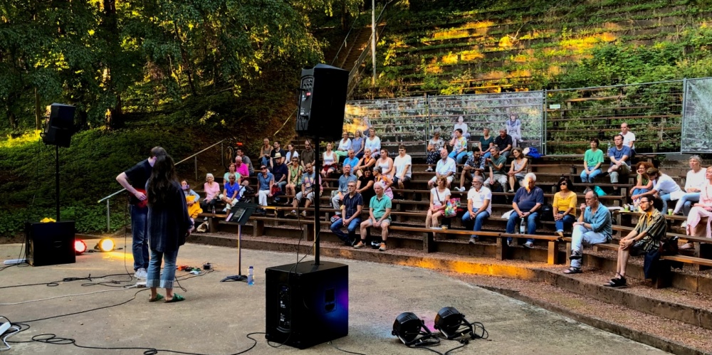 Bühne des Deutsch-Französischen Gartens, im Hintergrund sitzt das Publikum, links Sängerin und Gitarrist