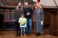 Kita - In den Hanfgärten Preisübergabe an die Kita in den Hanfgärten. Zu sehen ist ein Kinder welche die Urkunde hält und eine Betreuerin der Kita, sowie zwei Jurymitglieder.