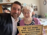 Zwei Personen lächeln und halten ein Schild in den Händen.