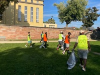Menschen in Warnwesten mit Mülltüten gehen über eine Wiese