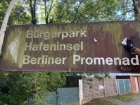 Schmutziges Schild mit dem Schriftzug "Bürgerpark Hafeninsel Berliner Promenade"