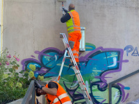 Zwei Männer in Warnkledung überstreichen Graffitis