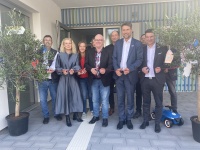 Mehrere Erwachsene stehen vor einem Gebäude an einem Band und Zerschneiden es als Symbol einer Eröffnung