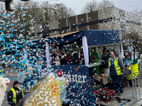 Konfetti fliegt durch die Luft vor einem fahrenden Umzugswagen, während Zuschauerinnen und Zuschauer am Straßenrand stehen.