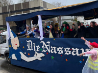 in Umzugswagen mit der Aufschrift „Die Nassauer“ fährt an den Zuschauern vorbei, während Menschen auf dem Wagen winken.