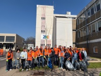 Gruppe von Menschen mit orangen Warnwesten und Müllsäcken steht vor einem Gebäude mit ZKE-Logo