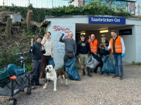 Gruppe von sieben Personen mit Müllsäcken und einem Hund vor einer Unterführung