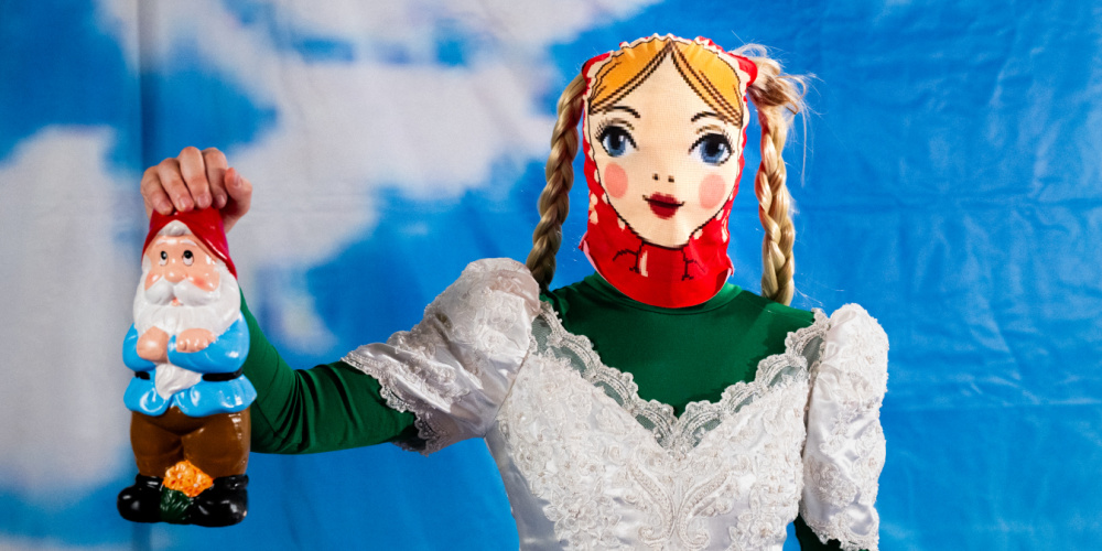 Ausstellung Top Quality Bitches Darja Linder Eine Person in einem Brautkleid trägt eine Matroschka-Maske und hält einen Gartenzwerg in der Hand